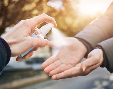 Erkek eli dezenfekte etmek için kadınların ellerine dezenfektan sıkarken çekilmiş yakın plan bir fotoğraf.