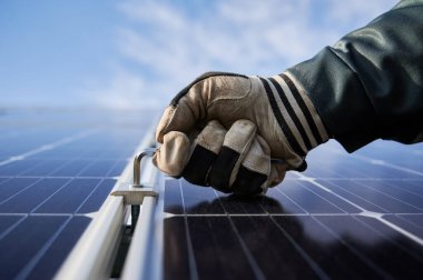Eldivenle eldiven üstüne uğursuz anahtar tutarak fotovoltaik güneş paneli yerleştirirken arka planda mavi gökyüzü vardı. Elektrikçi güneş fotovoltaik panel sistemini monte ediyor. Alternatif enerji kavramı