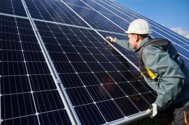 Kasklı adam teknisyen fotovoltaik güneş modülünü tamir ediyor. Eldivenli elektrikçi güneş fotovoltaik panel sistemini koruyor. Alternatif enerji ve güç sürdürülebilir kaynaklar kavramı.