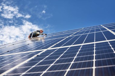 Kasklı erkek teknisyen bulutlu gökyüzünün altında mavi fotovoltaik güneş paneli kuruyor. Profesyonel işçi, tek başına güneş paneli kuruyor. Alternatif enerji kavramı