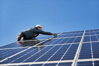 Güneş modüllerini, panelleri ve fotovoltaik güneş dizisini destekleyen erkek işçiler. Güvenlik kaskı ve eldiven takan bir elektrikçi. Güneş enerjisi ve gücü kavramı sürdürülebilir kaynaklar.
