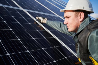 Koruyucu kostüm, kask ve eldiven giyen erkek işçilere yakın çekim. Elektrikçi güneşli bir günde fotovoltaik güneş pilleri kuruyor. Alternatif enerji ve güç sürdürülebilir kaynaklar kavramı.