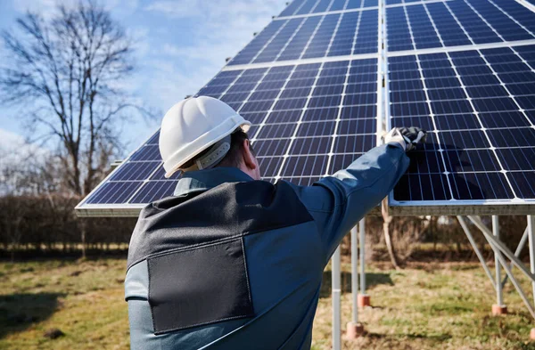 一个穿着工作服 头戴白色头盔 戴着工作手套 背对着相机站着 把太阳能组件绑在一起的工人的后视镜 可持续替代能源和电力的概念 — 图库照片