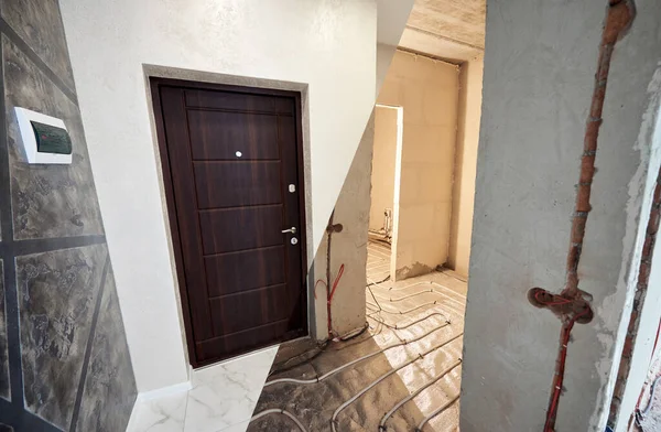 Modern apartment with front door before and after renovation. Comparison of old flat with underfloor heating pipes and new place with marble floor and brown entrance door.