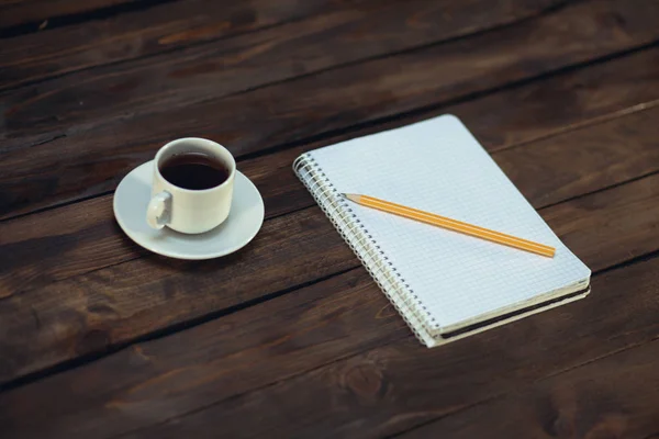 Notebook in pencil and cup of coffee on a wooden background