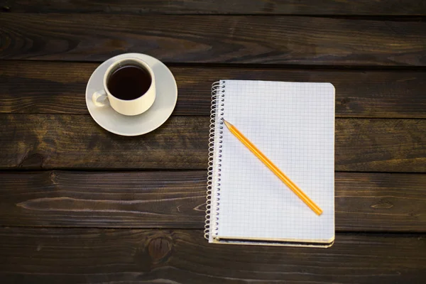 Notebook in pencil and cup of coffee on a wooden background — Stock Photo, Image