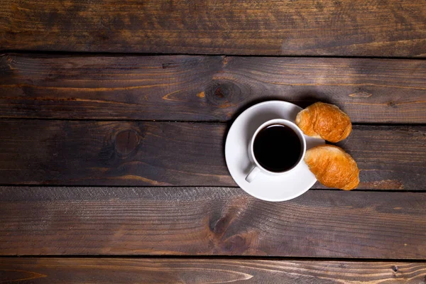 Caneca branca de café e um croissant em um fundo de madeira — Fotografia de Stock