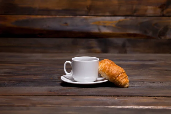 White mug of coffee and a croissant on a wooden background — Stock Photo, Image