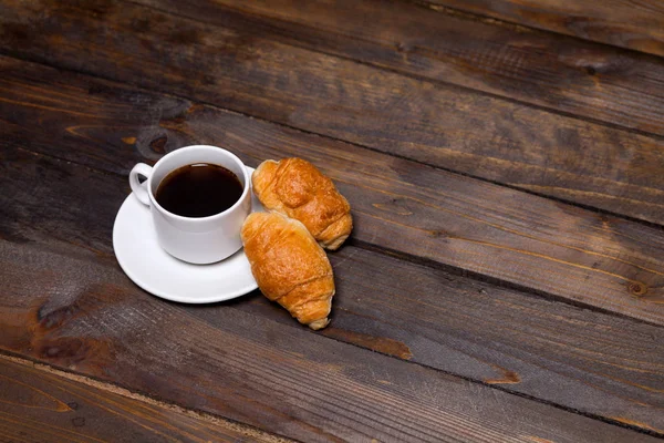 Caneca branca de café e um croissant em um fundo de madeira — Fotografia de Stock