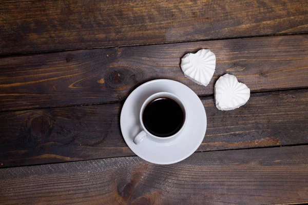 Caneca branca de café e dois marshmallows na forma de corações em um fundo de madeira para o café da manhã — Fotografia de Stock