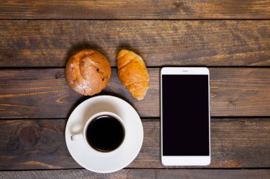 Hareket eden telefon ile beyaz bir fincan kahve ve kruvasan