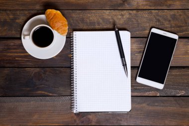 Yukarıdan görüntüleyin. Hareket eden telefon ile beyaz fincan kahve ve ahşap arka plan üstünde not etmek. Çalışma alanı düz yatıyordu.