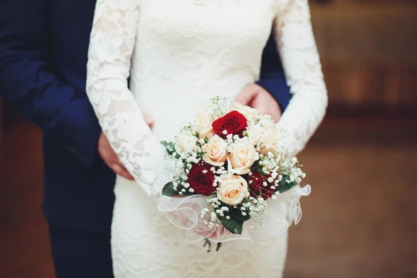 Pengantin pria memeluk pengantin wanita yang memegang karangan bunga, kembali di pernikahan — Stok Foto