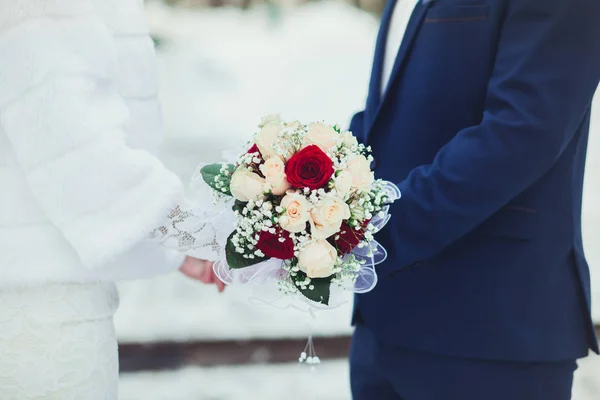 Pengantin pria dan wanita dengan karangan bunga untuk memegang lembut oleh tangan di pernikahan, close-up di musim dingin — Stok Foto