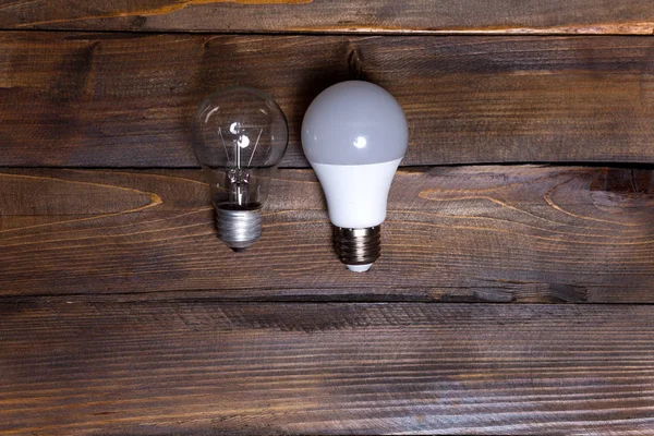 Two light bulbs. LED white and ordinary incandescent lamp on wooden background. Top view — Stock Photo, Image