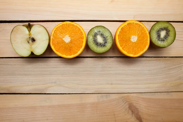 Half-cut green apple, kiwi, orange orange. Juicy fruit on wooden background