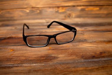 Ahşap arka planda siyah çerçeveli gözlükler, masa. Yukarıdan görüntüle