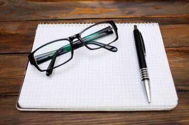 Beyaz sayfalar, cam gözlükler siyah çerçeve ve ahşap zemin üzerine kalem kutusu içinde not etmek. Üstten Görünüm