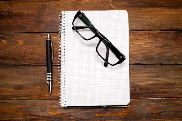 Notepad in box with white pages, glass spectacles in black frame and pen on wooden background. Top view — Stock Photo, Image