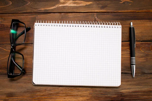 Notepad in box with white pages, glass spectacles in black frame and pen on wooden background. Top view — Stock Photo, Image