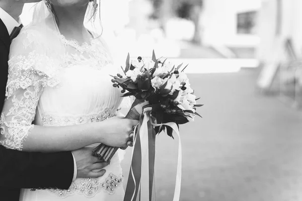 Pengantin pria memeluk pengantin wanita cantik dari belakang. Gadis itu memegang buket pernikahan di tangannya. Fotografi hitam putih — Stok Foto