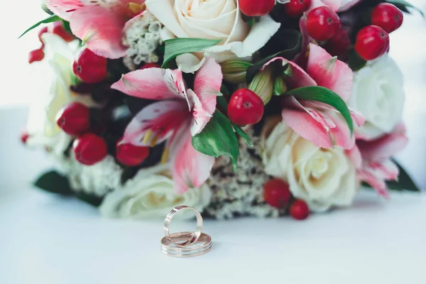 着一束美丽的鲜花的新娘的白色桌子上的黄金结婚戒指。 — 图库照片