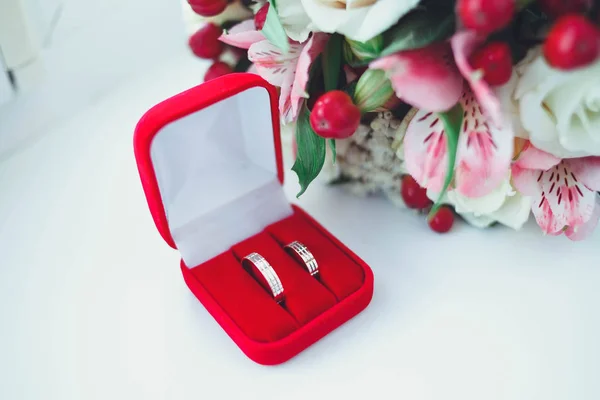 Gold wedding rings on a white table with a bouquet of brides from beautiful flowers — Stock Photo, Image