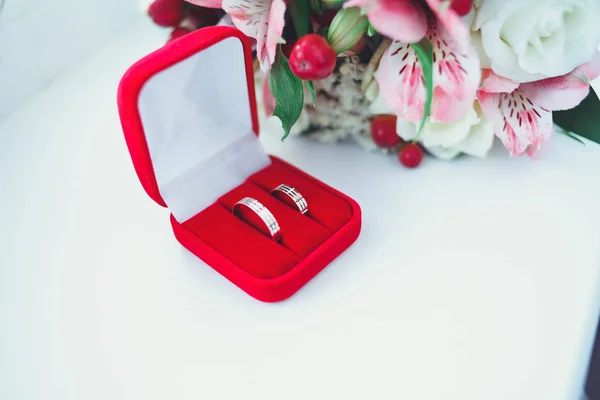 Gold wedding rings on a white table with a bouquet of brides from beautiful flowers — Stock Photo, Image