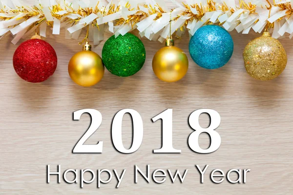 Bright colored New Year's balls and a garland on a light wooden background with the inscription Happy New Year 2018 — Stock Photo, Image