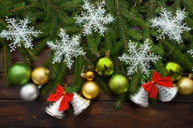 Green living spruce branches on a dark wooden background. New Year background with beautiful balls and white snow and bells. Top view clipart