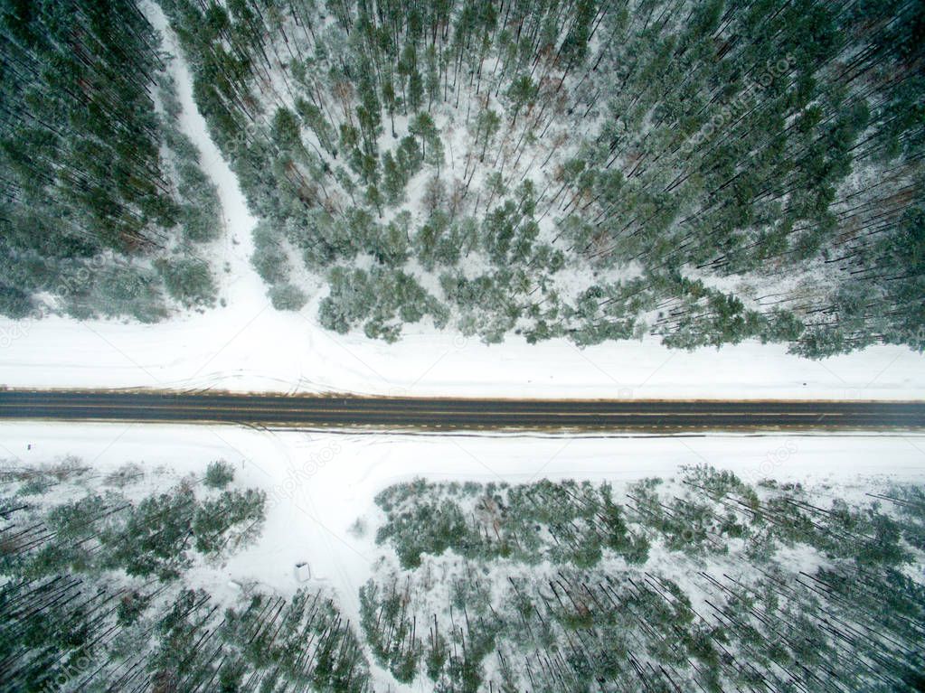Winter forest and asphalt road. View from above. The photo was taken with a drone. Pine and spruce forest with a black road in the snow.