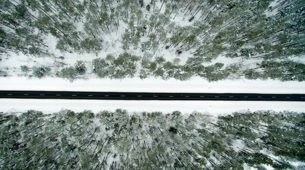 겨울 숲과 아스팔트도 로입니다. 위에서 볼 수 있습니다. 사진은 무인 항공기와 함께 찍은. 눈에 소나무와 전나무 숲 — 스톡 사진