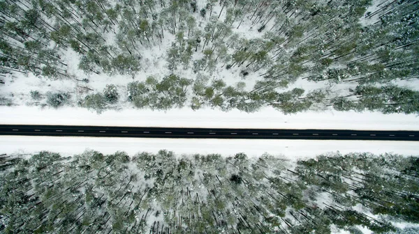 Winterwald und Asphaltstraße. Blick von oben. Das Foto wurde mit einer Drohne aufgenommen. Kiefern- und Tannenwald im Schnee — Stockfoto