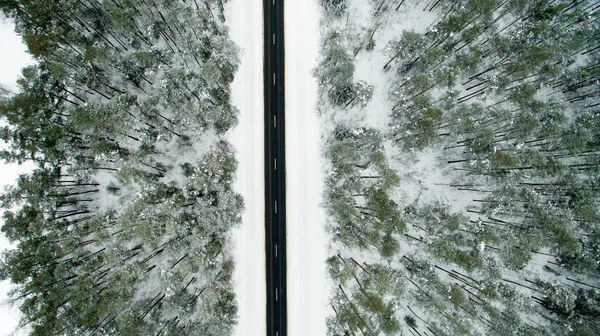 Floresta de inverno e estrada de asfalto. Vista de cima. A foto foi tirada com um drone. Floresta de pinheiro e abeto na neve — Fotografia de Stock