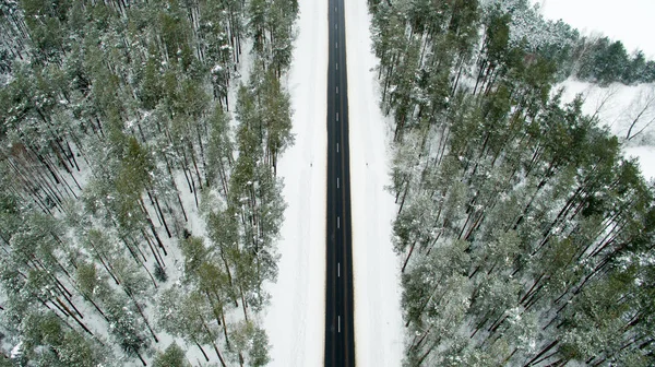 Floresta de inverno e estrada de asfalto. Vista de cima. A foto foi tirada com um drone. Floresta de pinheiro e abeto na neve — Fotografia de Stock