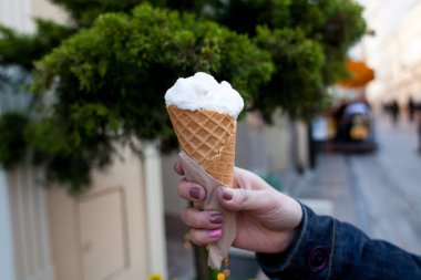 Bir kız, bulanık yeşil arka planda bir waffle bardağın içinde beyaz bir dondurma tutuyor. Yaz fotoğrafı yakın çekim.