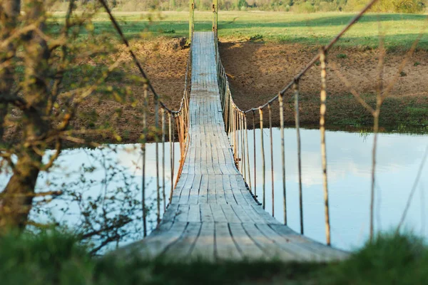 Old suspended wooden foot bridge over the river. Photo on a summer day. River crossing for people