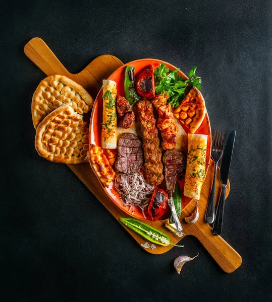 Berbagai kebab dengan sayuran dan roti datar di papan kayu besar dengan latar belakang gelap — Stok Foto