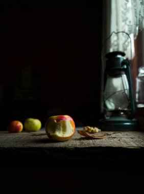 Still life with apples, fallen leaf and lantern on old wooden table by window clipart