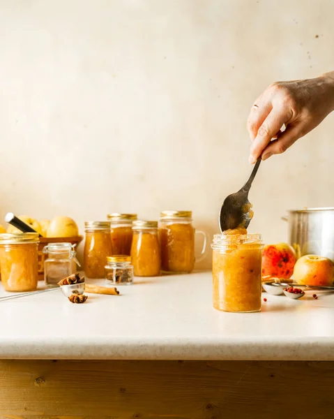 Mutfak masasındaki cam kavanozlarda ev yapımı elma sosu kaşıklayan bir kadın. — Stok fotoğraf