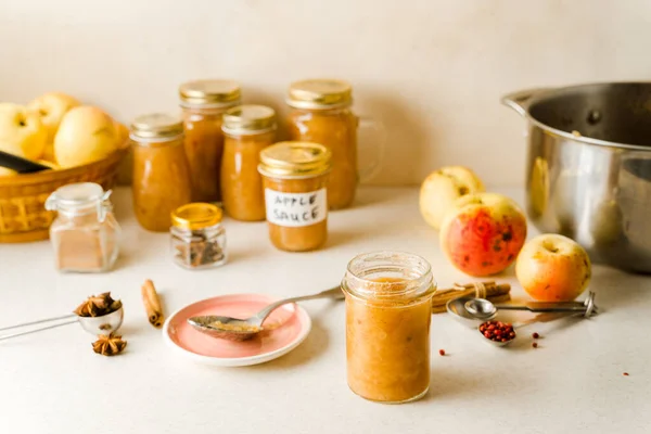 Cam kavanozlarda, malzemelerde, mutfak masasında tabak ve kaşıkta taze pişmiş elma püresi. — Stok fotoğraf