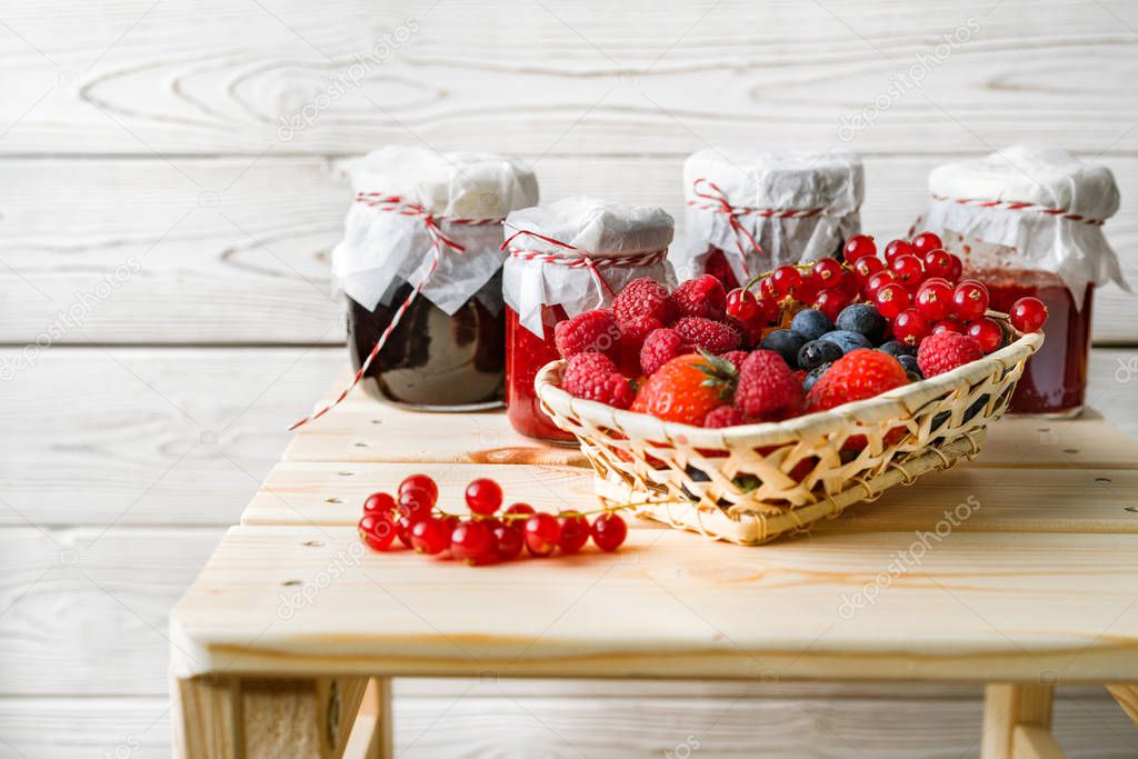 Assorted berries in a basket, glass jars with jams from different berries