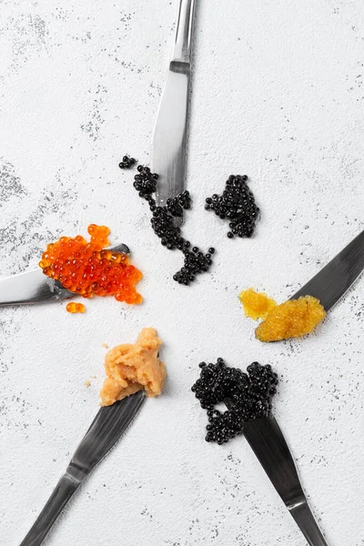 Cuchillos con diferentes tipos de caviar sobre fondo blanco — Foto de Stock