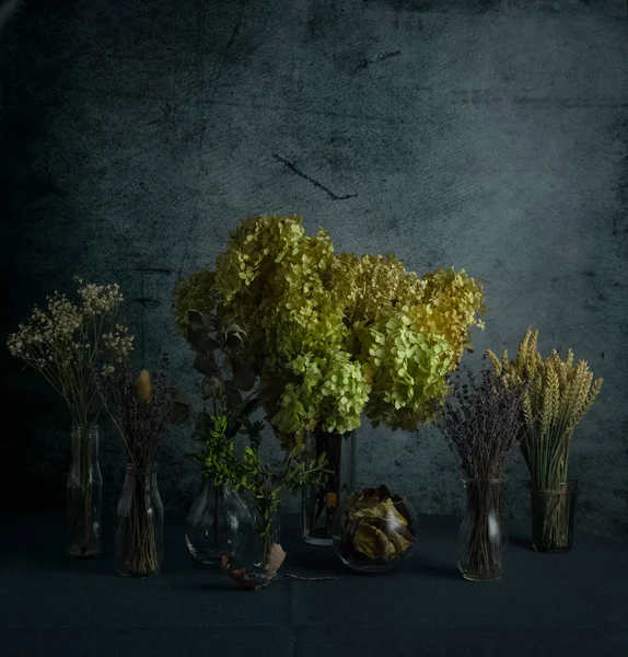 Still life image of dried flowers and plants in glass bottles on dark blue grunge background — Stock Photo, Image