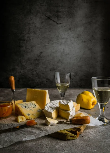 Low key still life with various cheeses, wine in glasses, quince fruit, and jam, with copy space