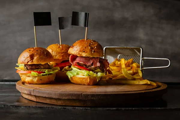 Selección de hamburguesas y una porción de papas fritas servidas sobre tabla de madera — Foto de Stock