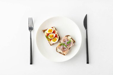 Danish smorrebrod open sandwiches on white plate, fork and knife on white background