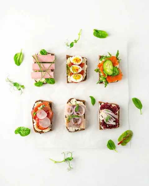 Selection of Danish smorrebrod open sandwiches, green salad leaves on parchment paper on white background — Stockfoto