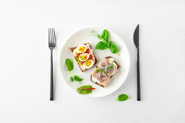 Danish smorrebrod open sandwiches on white plate, fork and knife, green salad leaves on white background — Stok fotoğraf