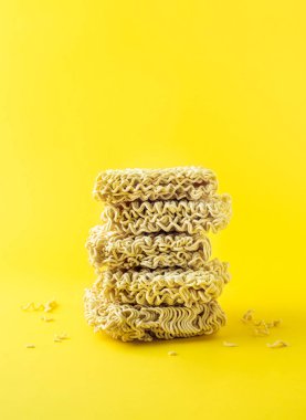 Stacked dry instant noodles blocks on vibrant yellow background